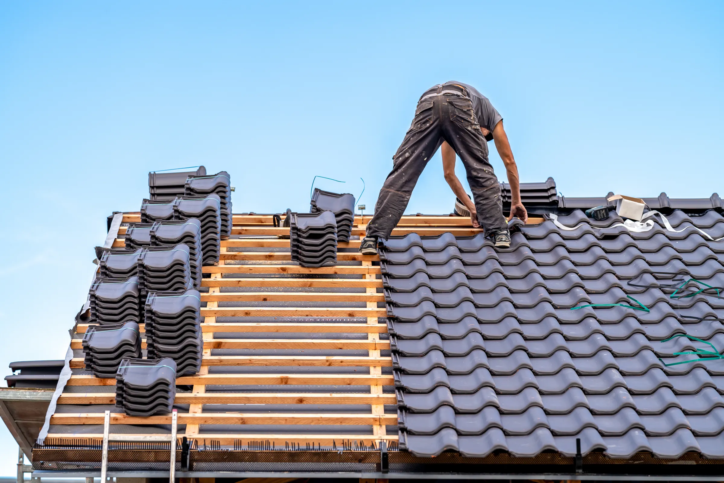 Roofer laying interlocking roof tiles on battens