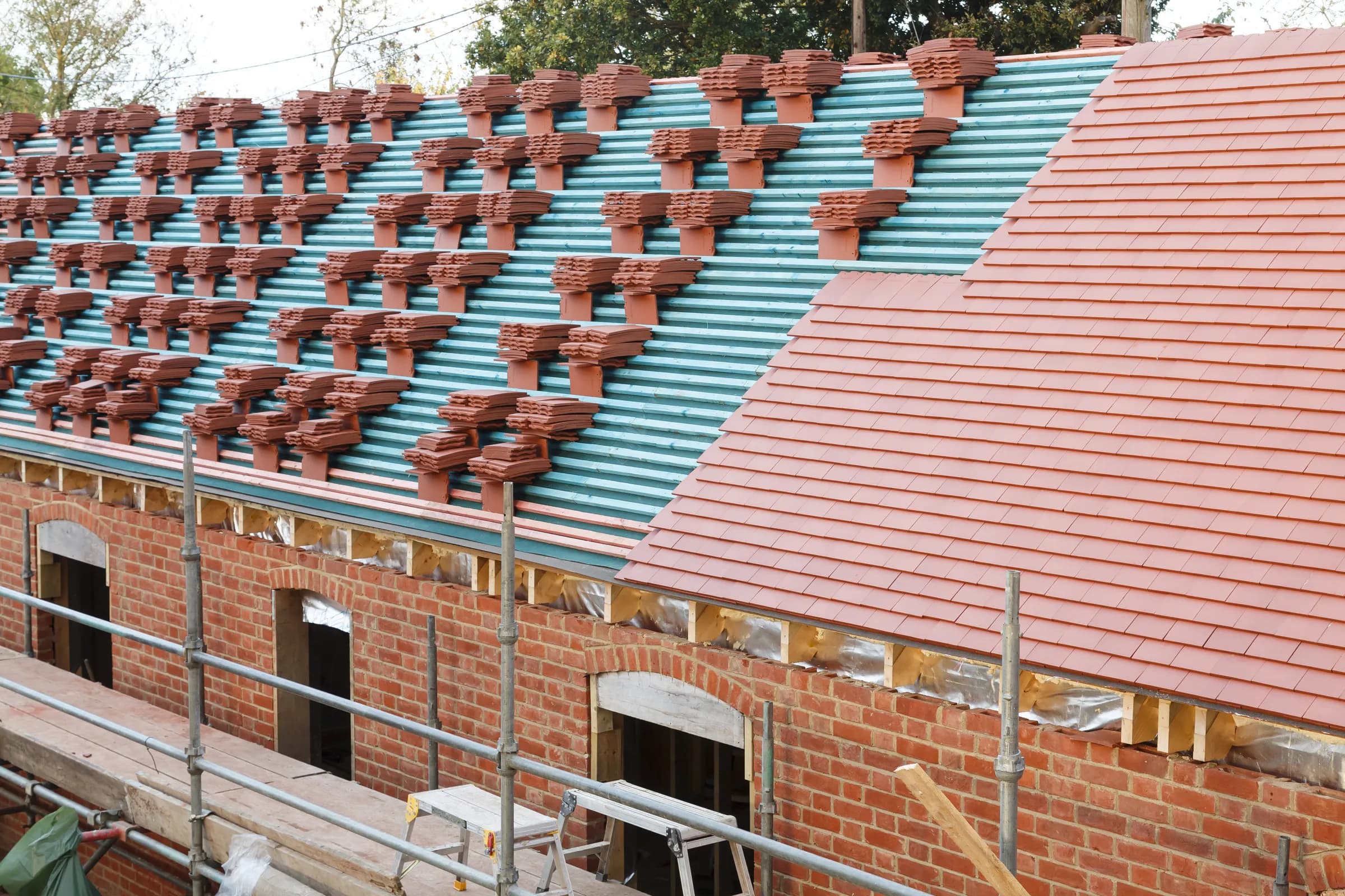 Pitched tile roof under construction on a scaffolded brick building